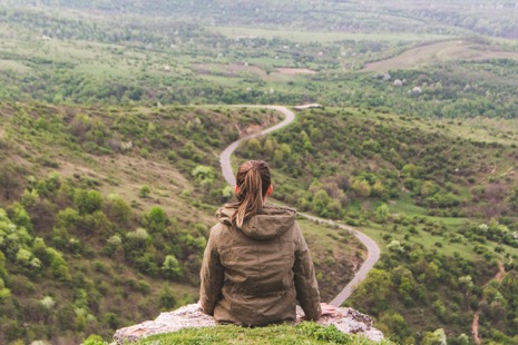 Photo of girl sitting atop a clif looking down on a road